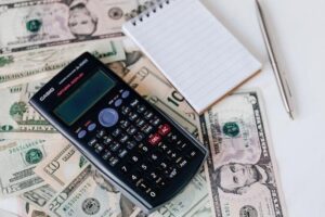A calculator on top of dollar bills with a notepad beside it